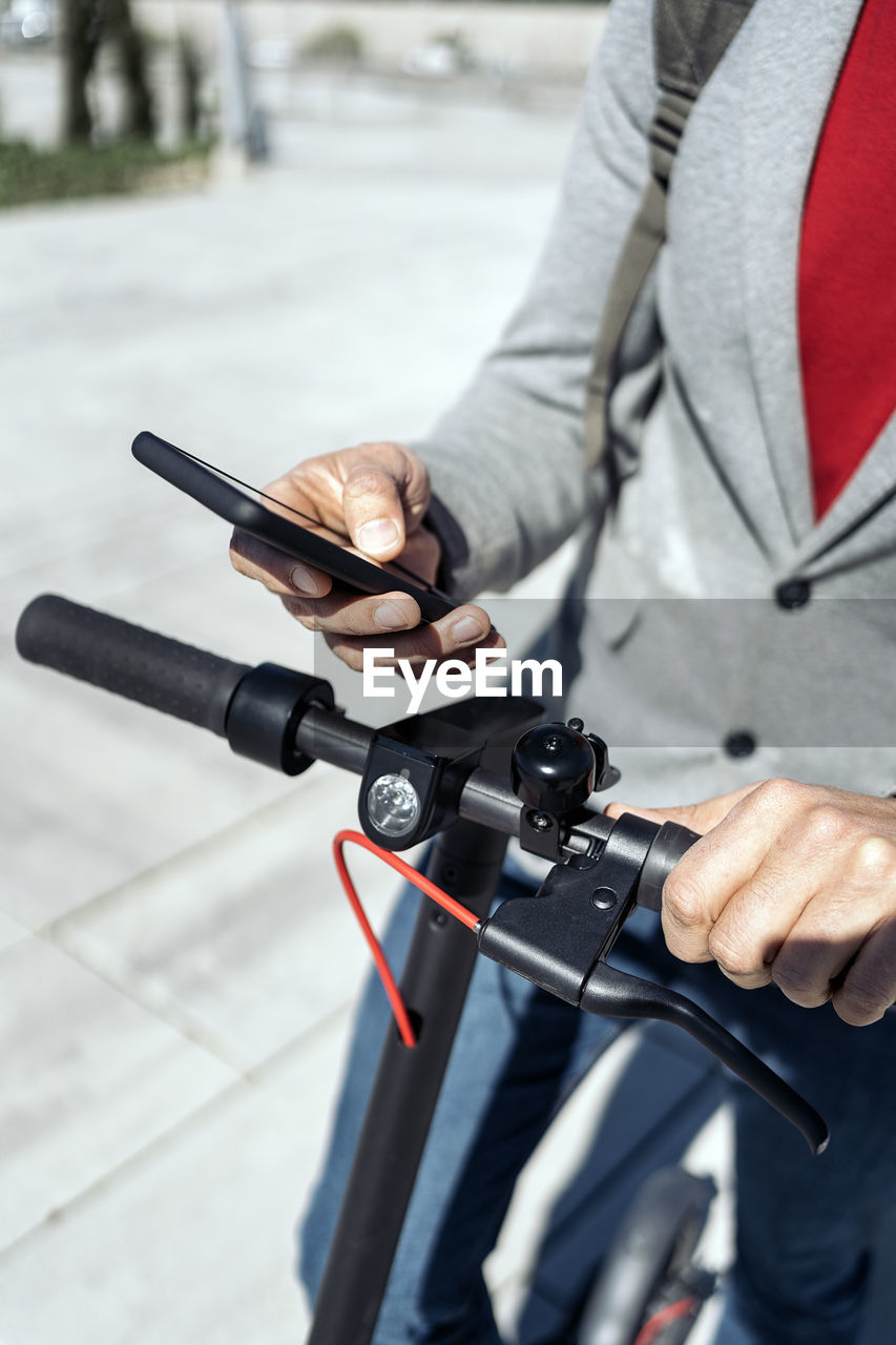 Midsection of businessman using mobile phone while standing with push scooter