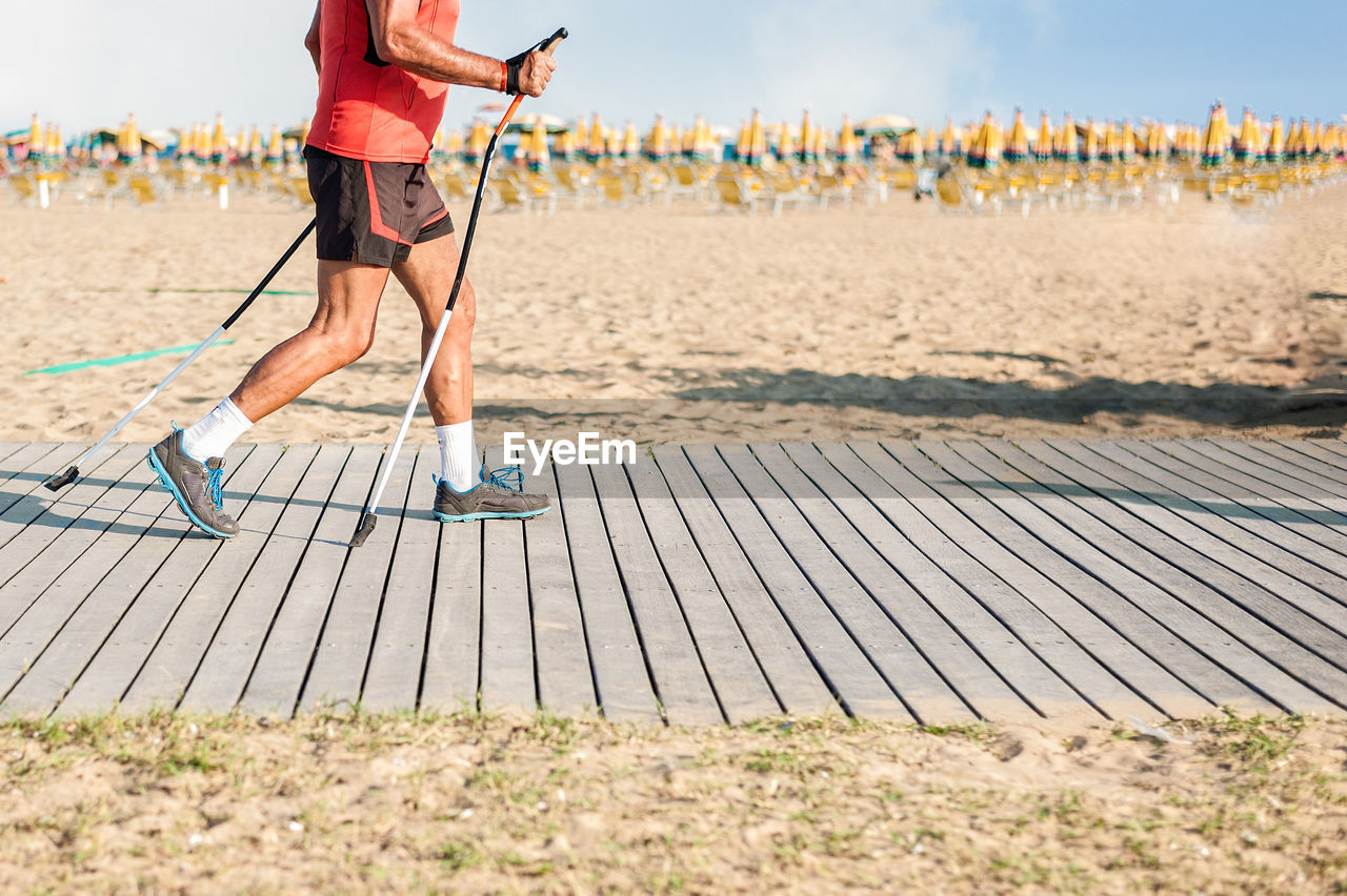 Low section of hiker walking on boardwalk against sky