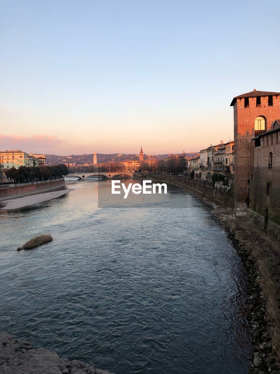 Bridge over river against buildings during sunset