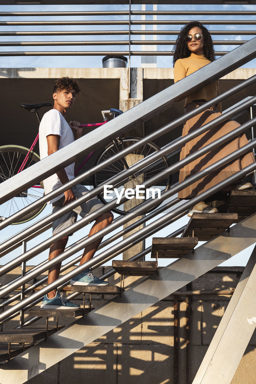 Young couple climbing stairs, carrying bicycle