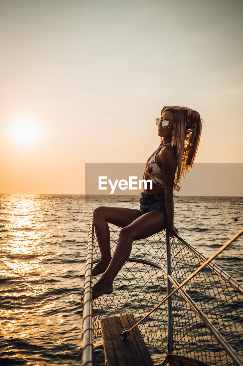 WOMAN WITH ARMS RAISED AGAINST SEA DURING SUNSET