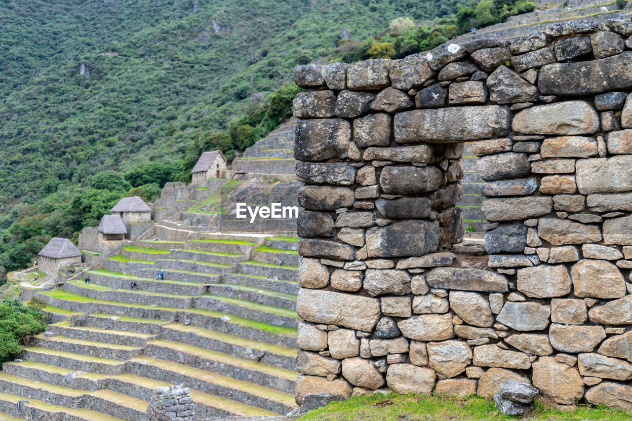 Stone wall and window overlooking inca terraces and huts at machu picchu, peru