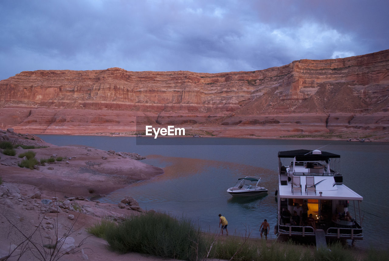 Ferry moored in lake powell by rocky mountains against cloudy sky