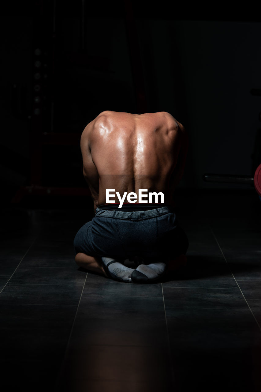 REAR VIEW OF SHIRTLESS MAN RELAXING ON FLOOR