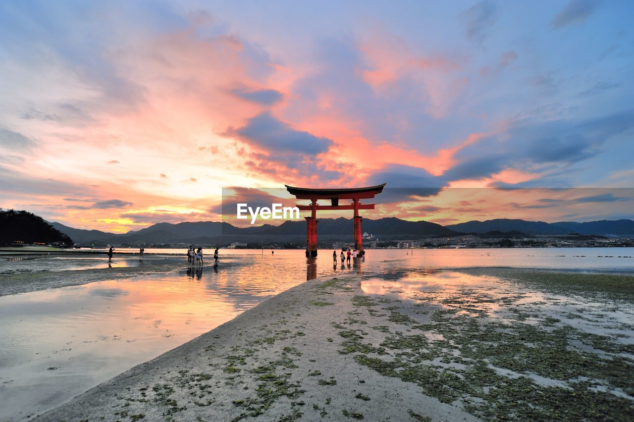 Torii gate in sea at itsukushima shrine against sky during sunset