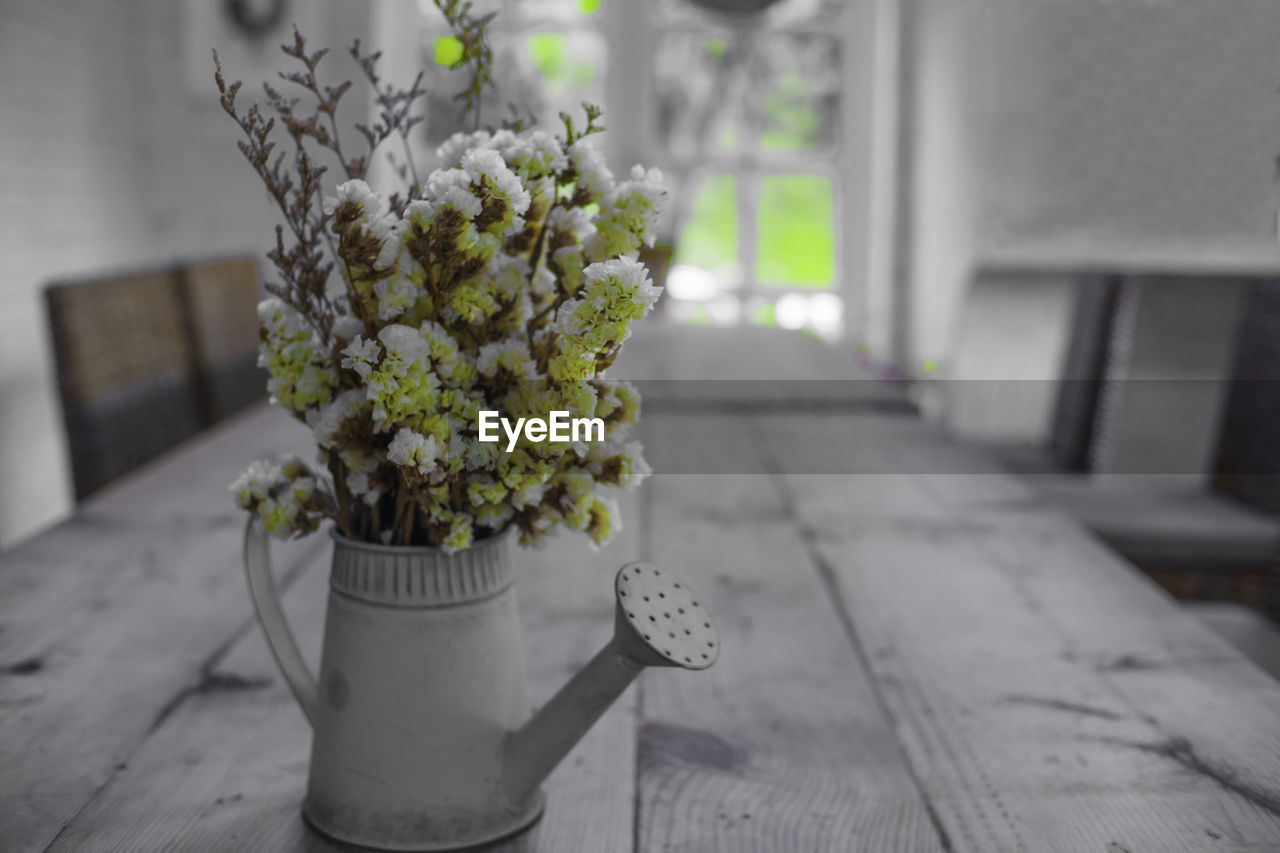 Small yellow flowers in vase on the wooden table - can be used as blurred background without focus