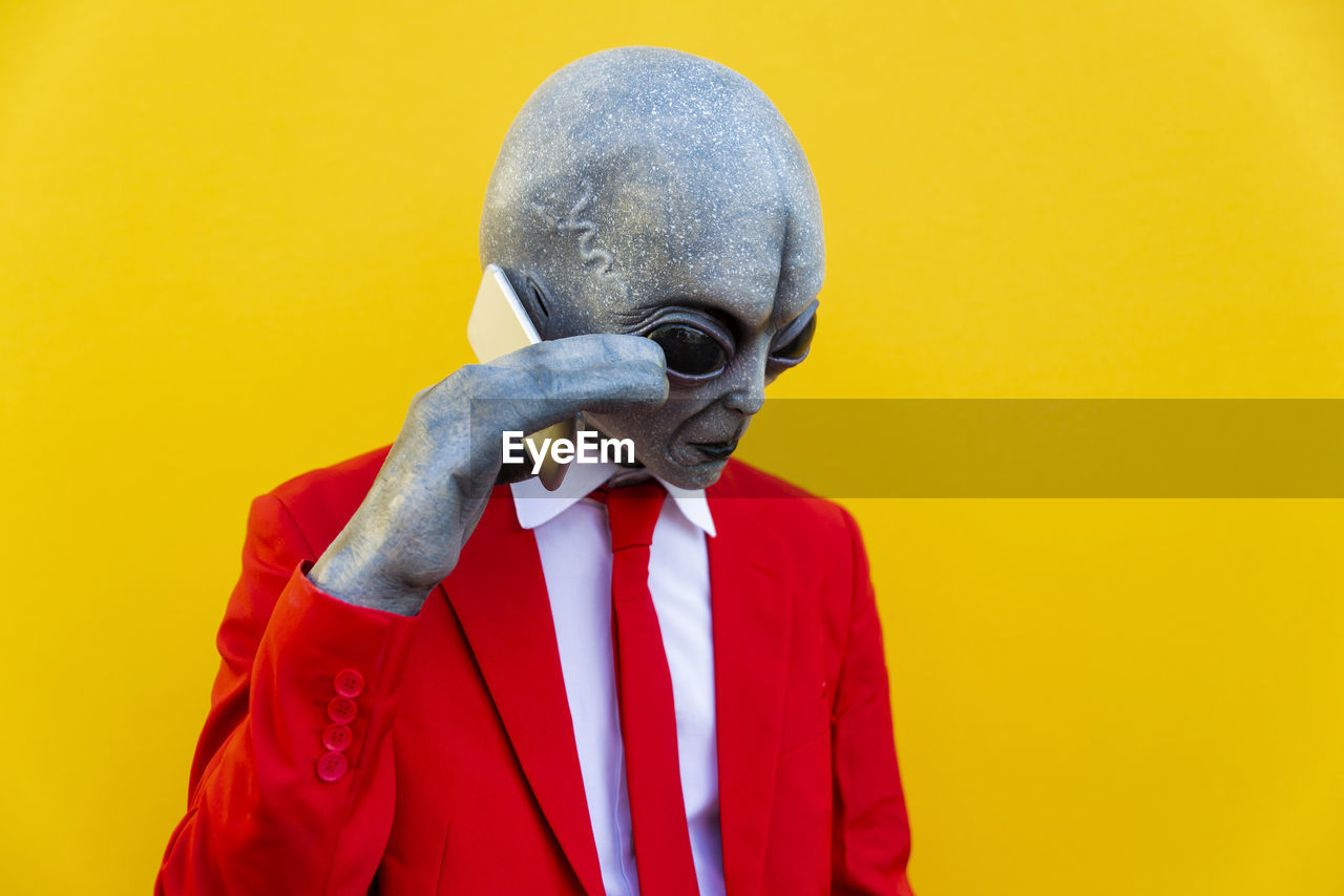 Portrait of man wearing alien costume and bright red suit using smart phone