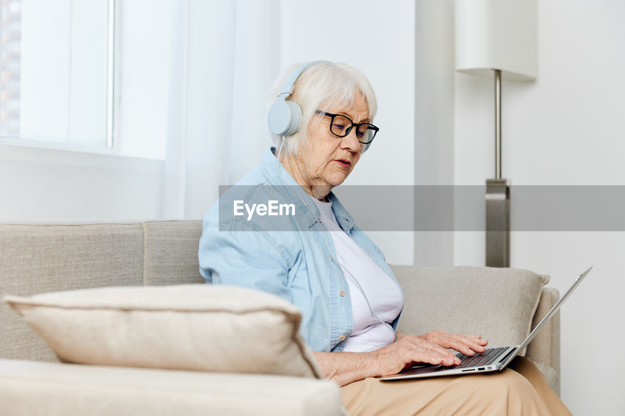 portrait of young woman using laptop while sitting on sofa at home