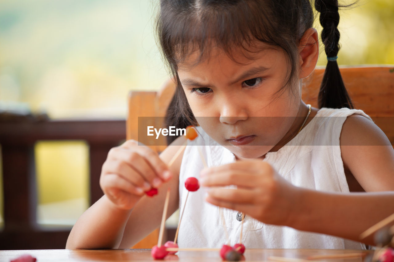 Cute girl making molecule model on wooden table in porch