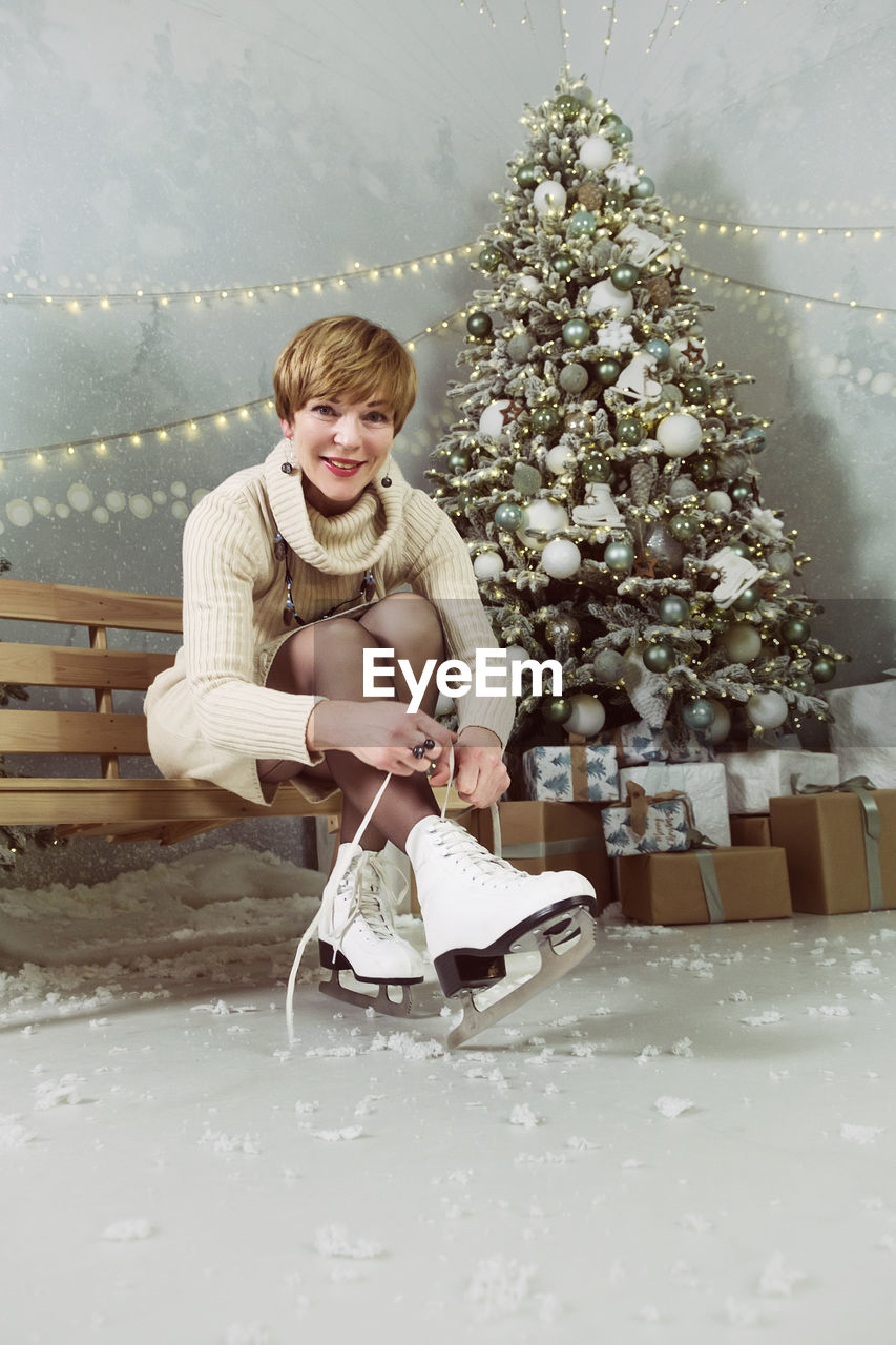 An adult woman in the new year at the skating rink ties her skates  next to the christmas tree