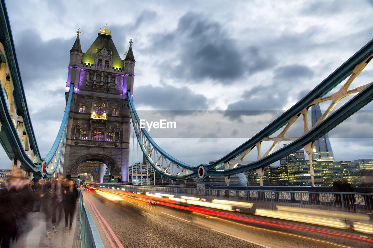 Light trails on suspension bridge against cloudy sky