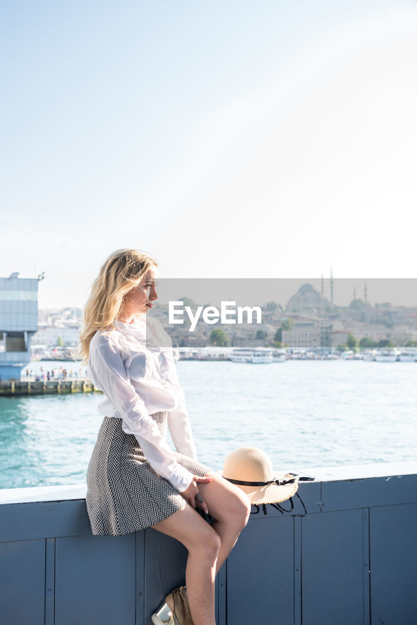 Woman sitting on railing of ship in sea against sky