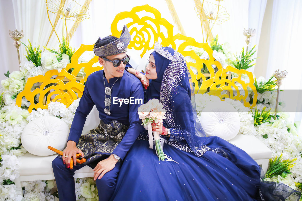 Bride and groom looking at each other while sitting on sofa