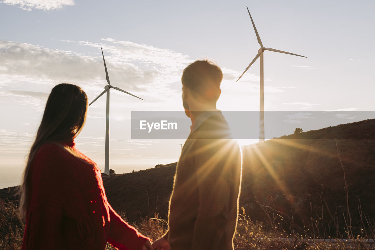 Couple holding hands looking at wind park at sunset