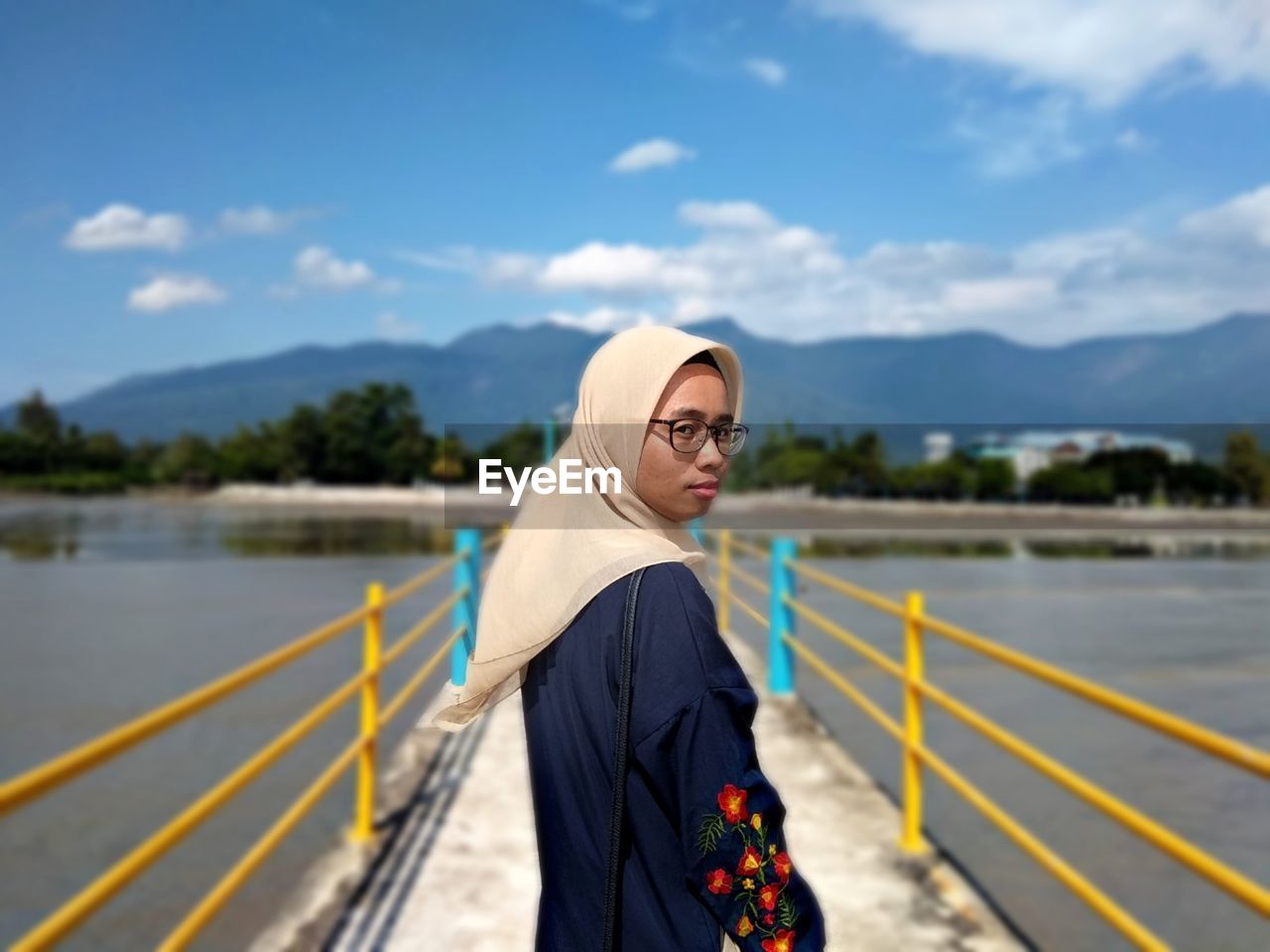 Portrait of woman standing on bridge over lake against sky