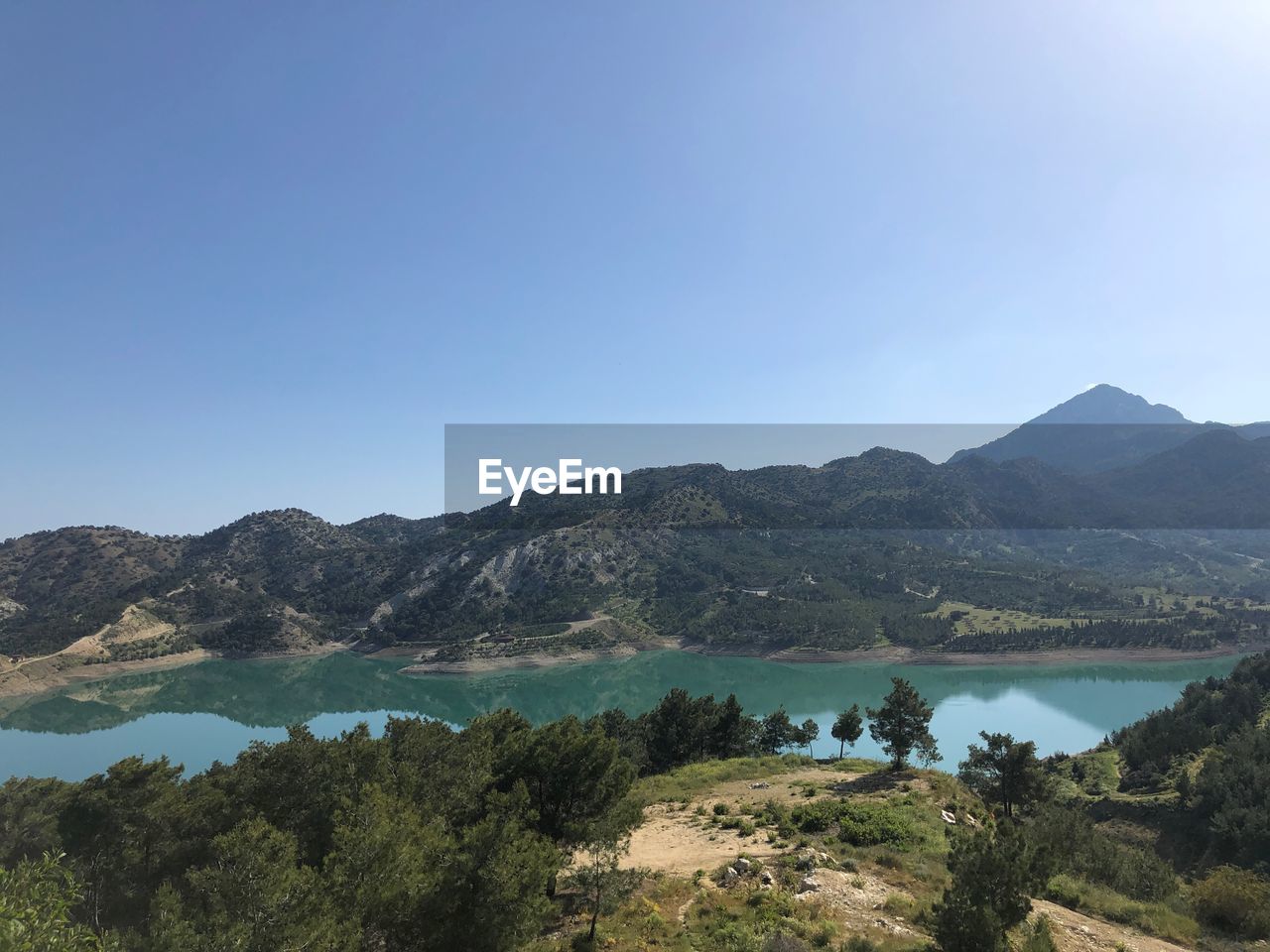 Scenic view of lake and mountains against clear blue sky