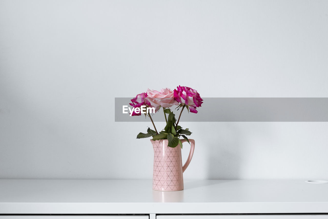 Pink flowers in vase on table against wall