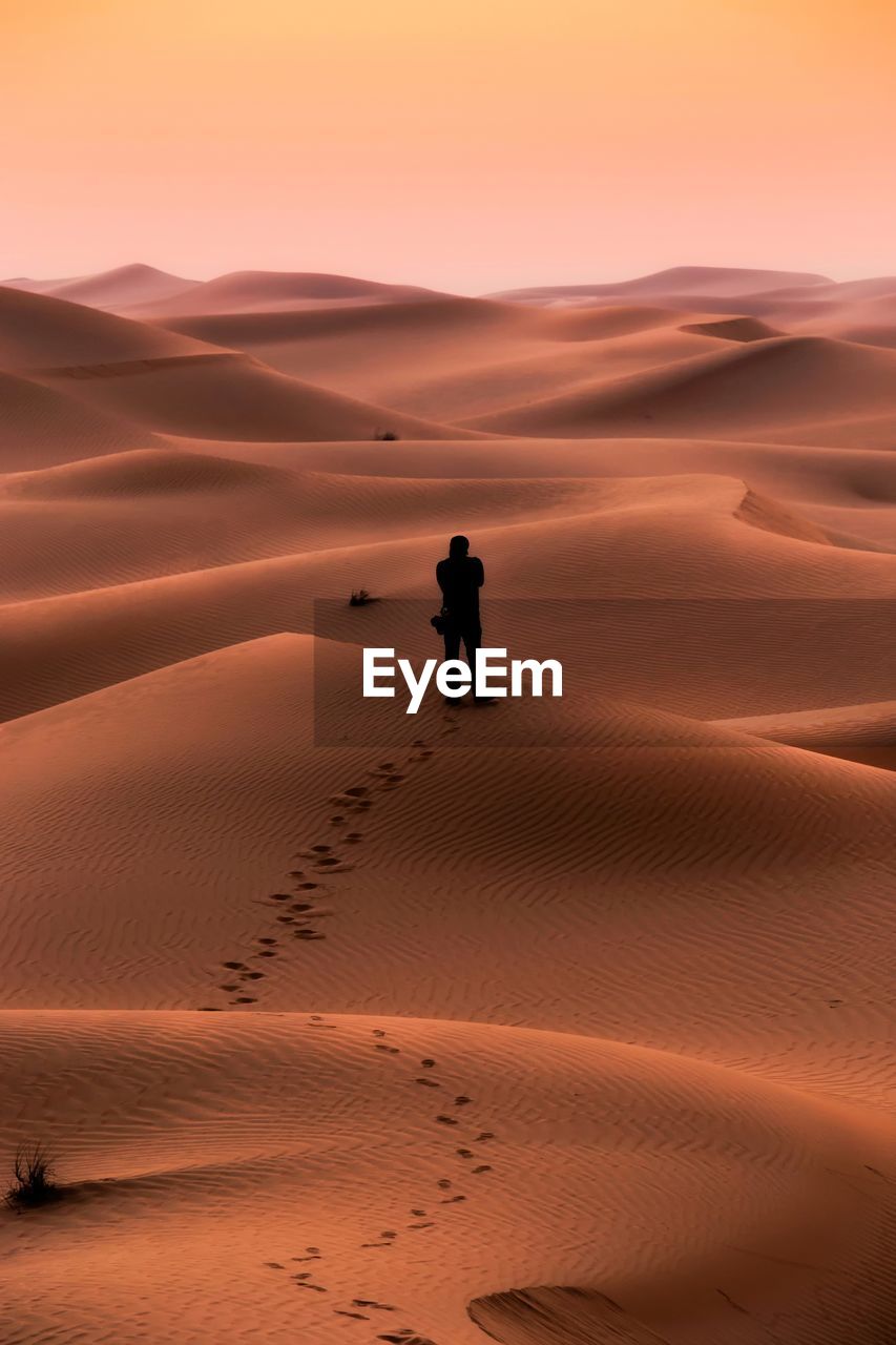 Mid distance view of silhouette man standing at desert during sunset