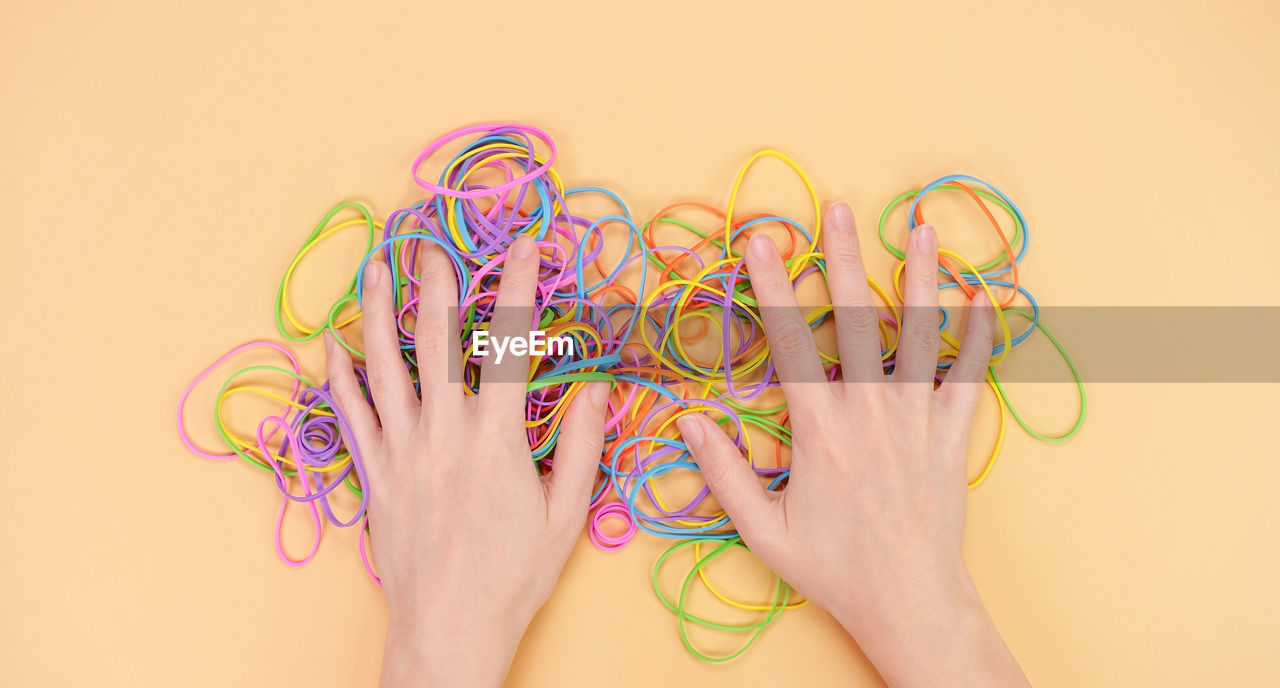 Hands hiding colored rubber bands on yellow background 