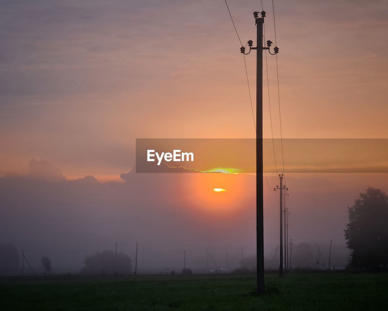 SILHOUETTE ELECTRICITY PYLONS ON FIELD AGAINST ORANGE SKY