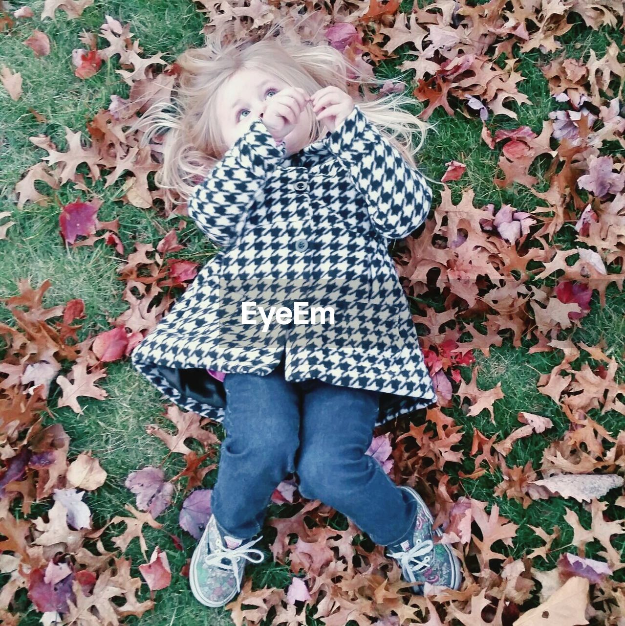 Full length of cute girl relaxing on field in park during autumn