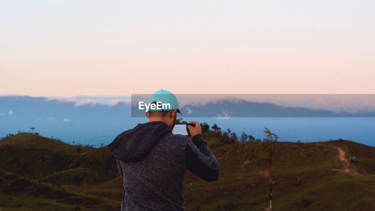 Rear view of man photographing mountain during sunset