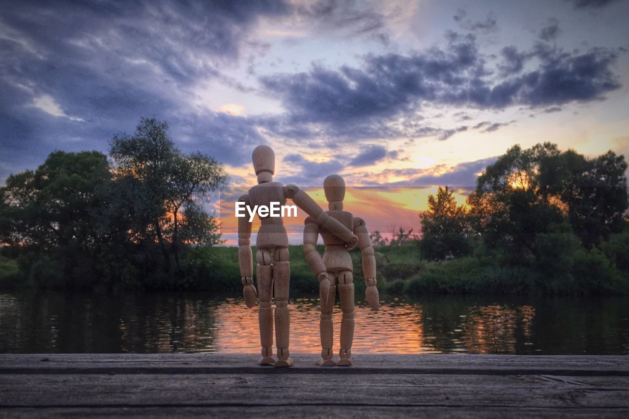 Wooden figurines by lake during sunset