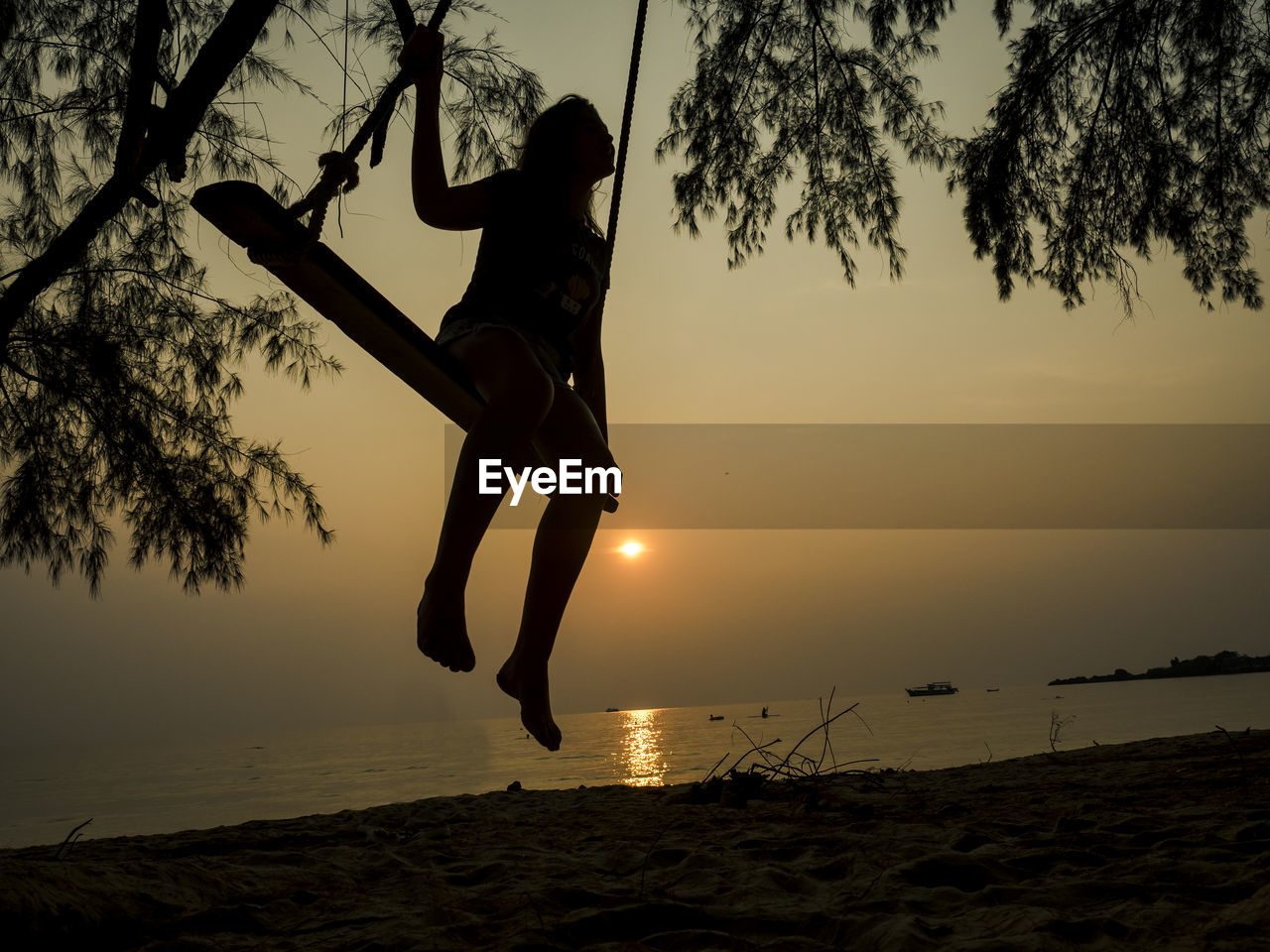 Silhouette girl swinging at beach against sky during sunset