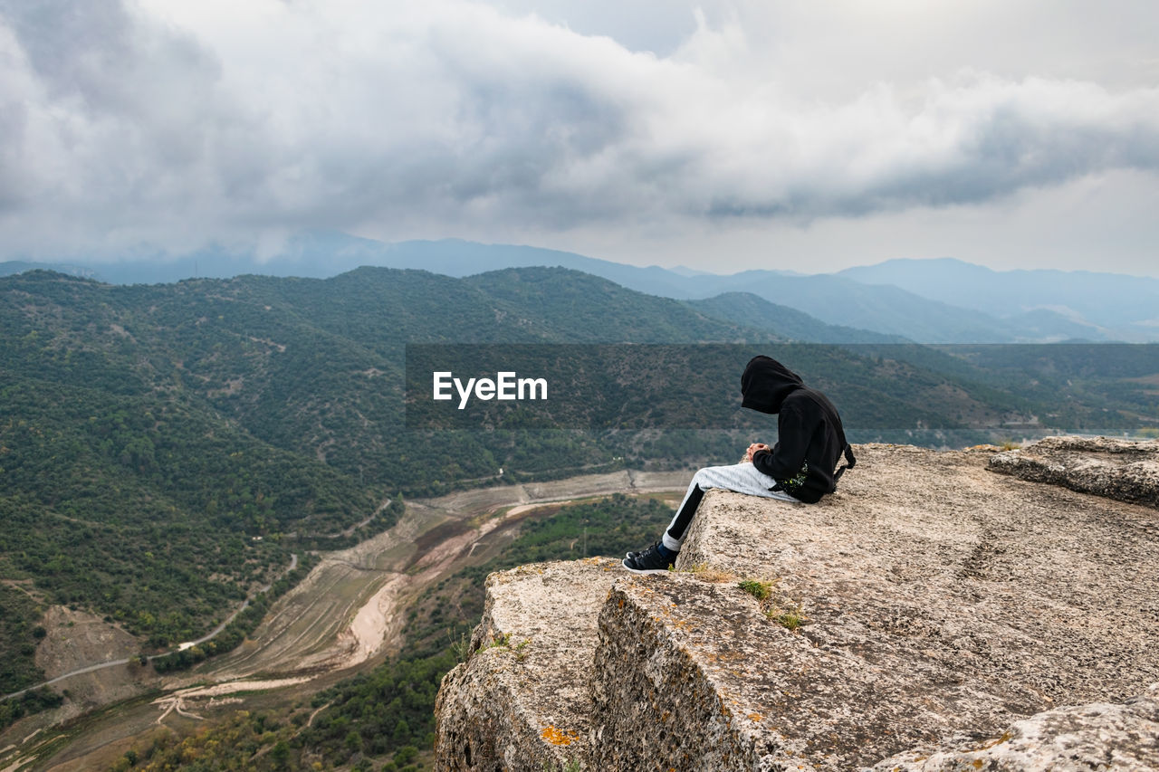 Teenager sit down sat on the edge of a cliff while storm is coming