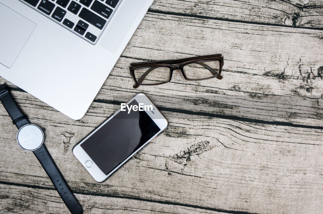 High angle view of laptop by mobile phone and eyeglasses with wristwatch on table