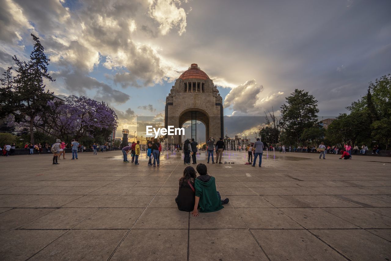 Tourists in front of building against cloudy sky