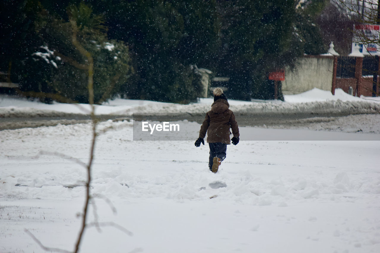 Full length rear view of boy walking on snow