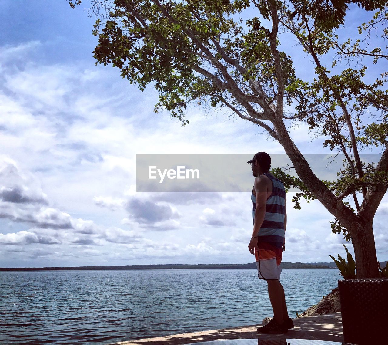 Mid adult man standing on retaining wall by lake against sky