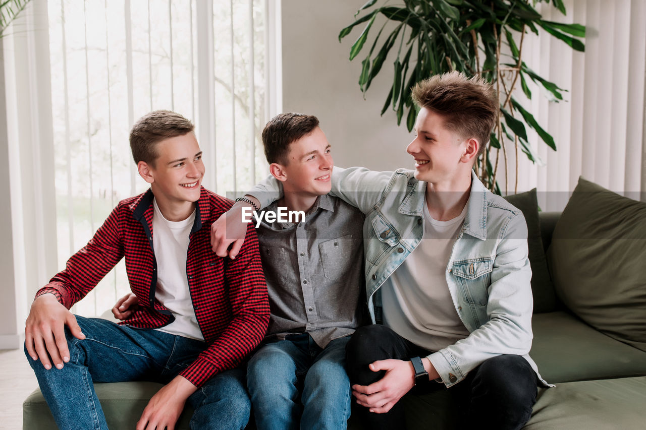 Three male friends are talking at the green sofa in living room. gossip teens hug each other