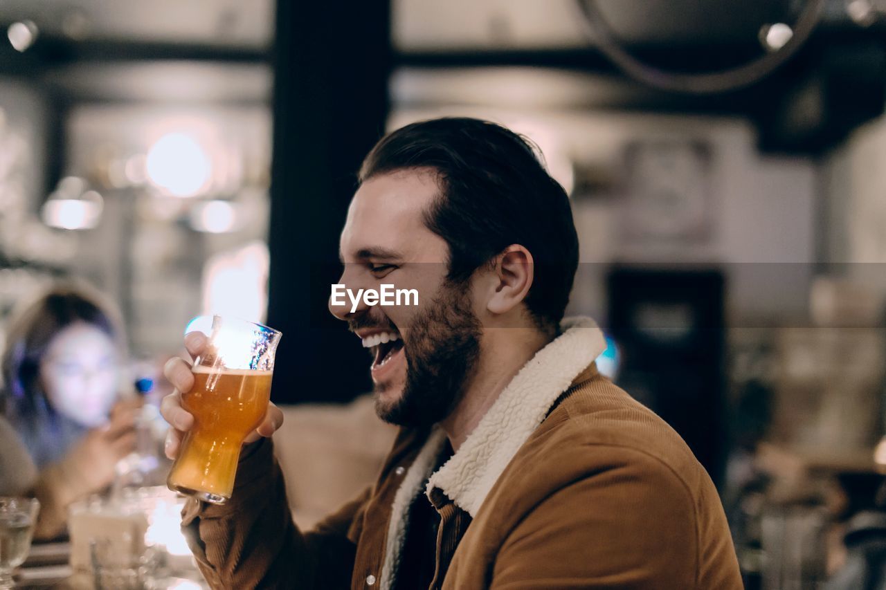 Man holding beer glass laughing while sitting in restaurant