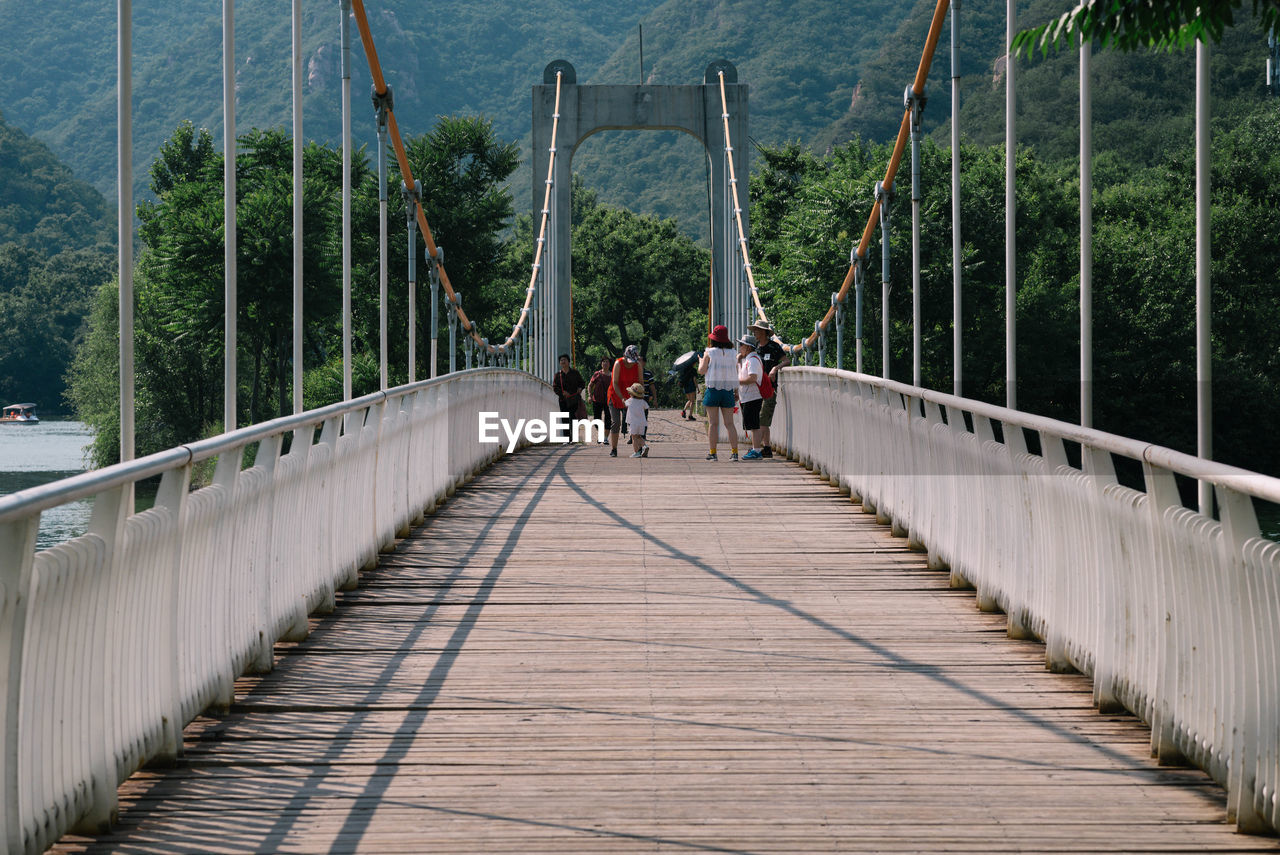 PEOPLE WALKING ON FOOTBRIDGE AGAINST PLANTS