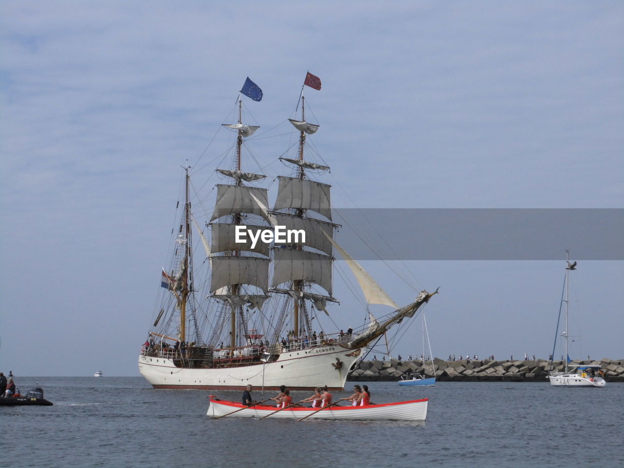 Women rowing boat by ship in sea against sky