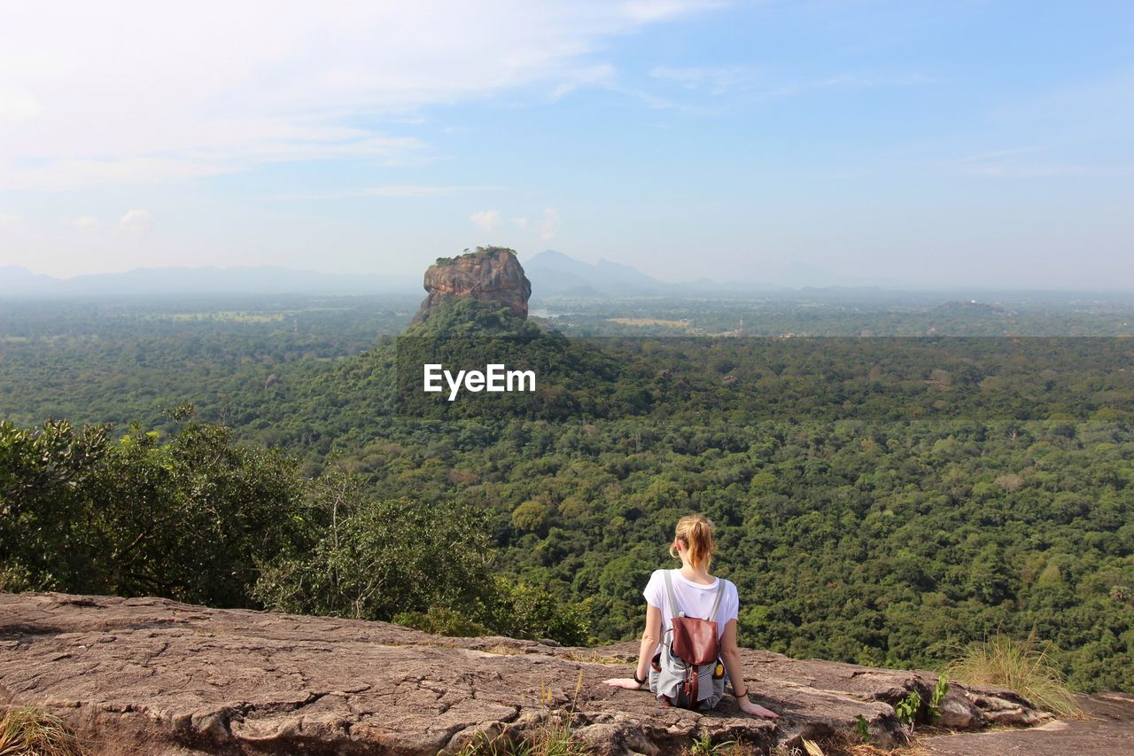 Rear view of woman sitting on mountain against sky