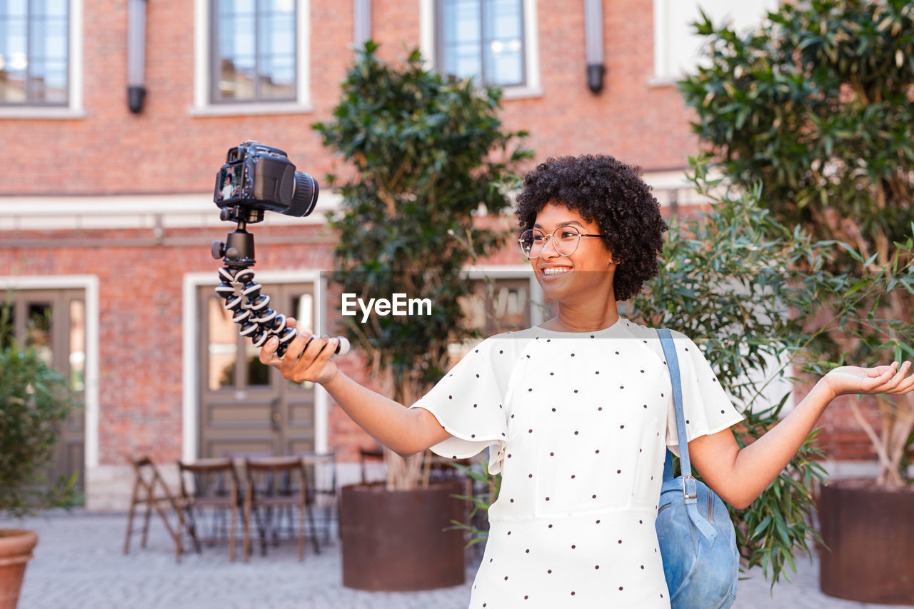 Smiling girl taking selfie through monopod against brick wall