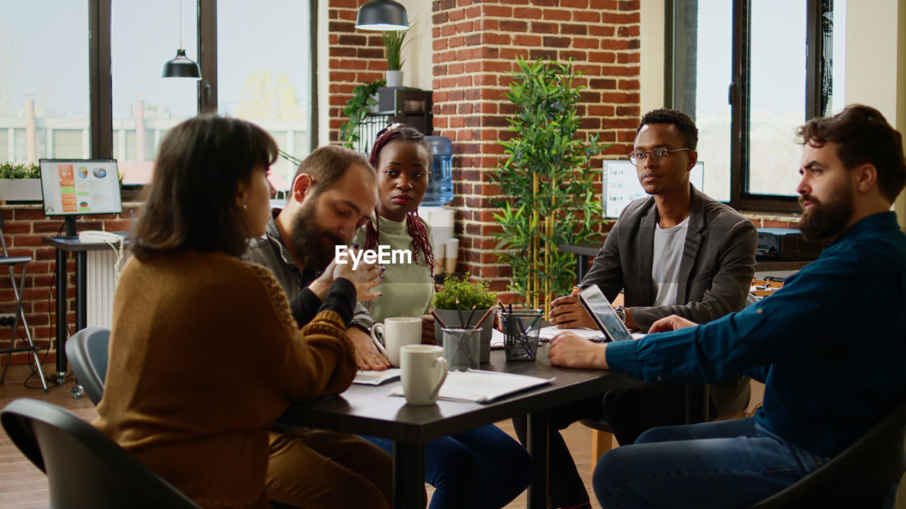 portrait of smiling friends using mobile phone while sitting at restaurant