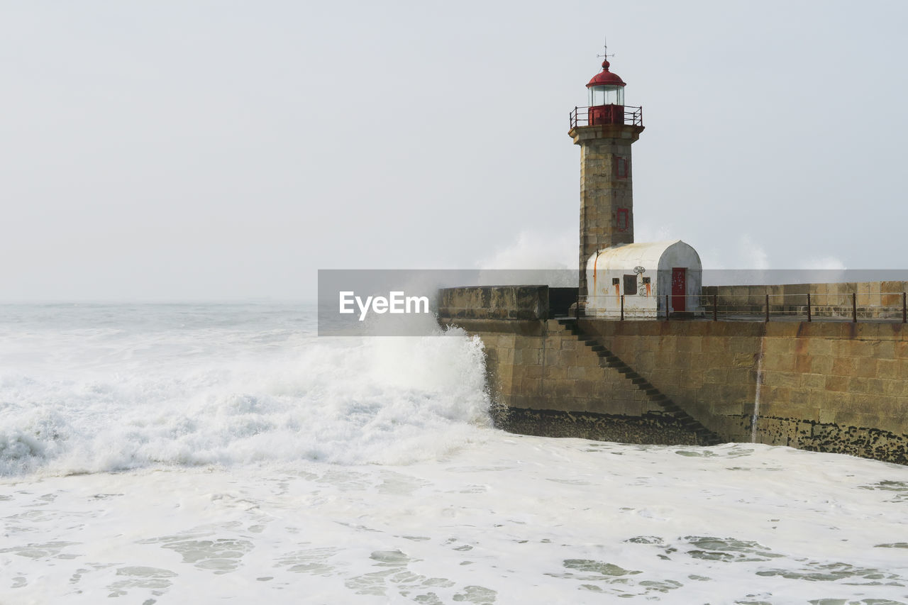 LIGHTHOUSE BY SEA AGAINST BUILDING