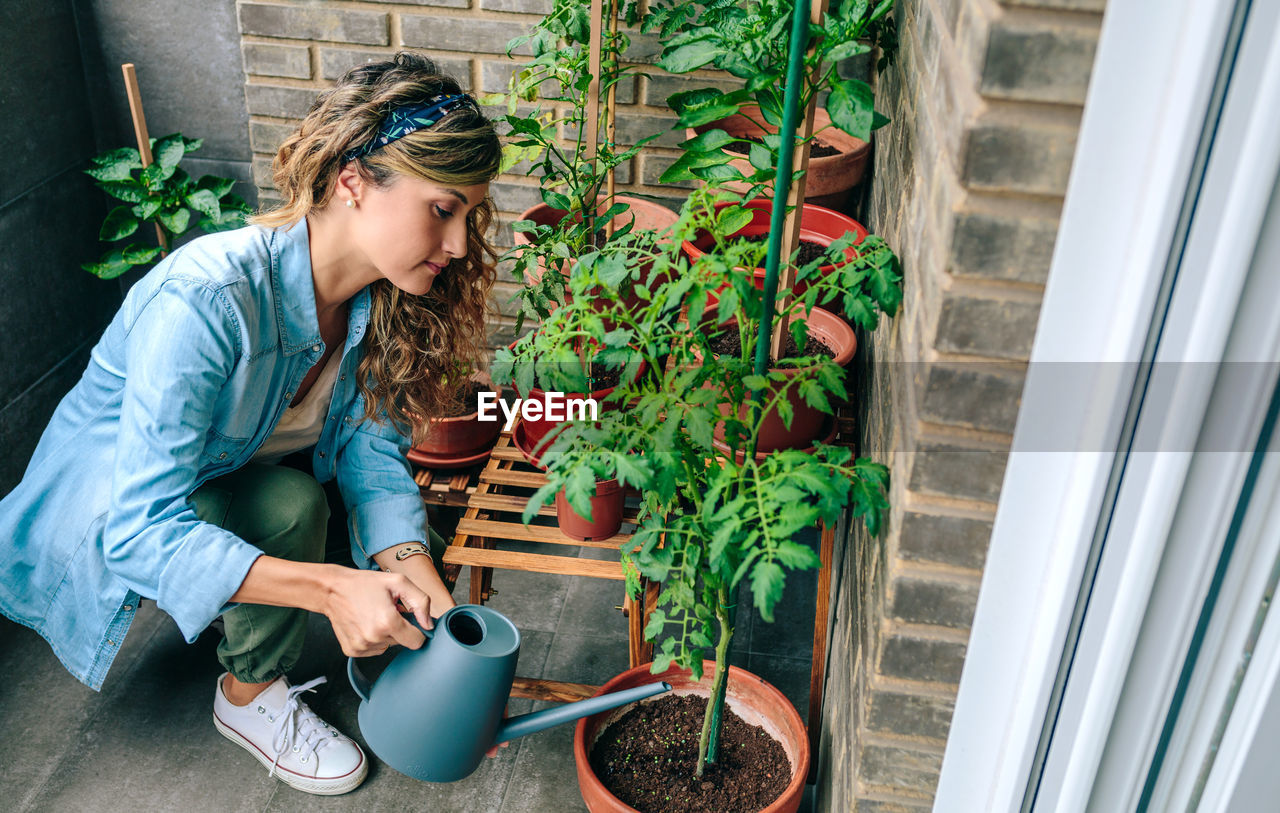 Woman using watering can with plants of urban garden on terrace