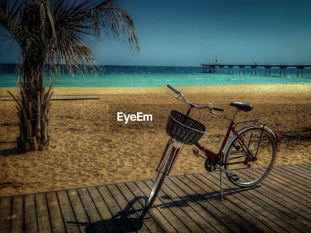 Bicycle parked on boardwalk in front of sea against clear sky