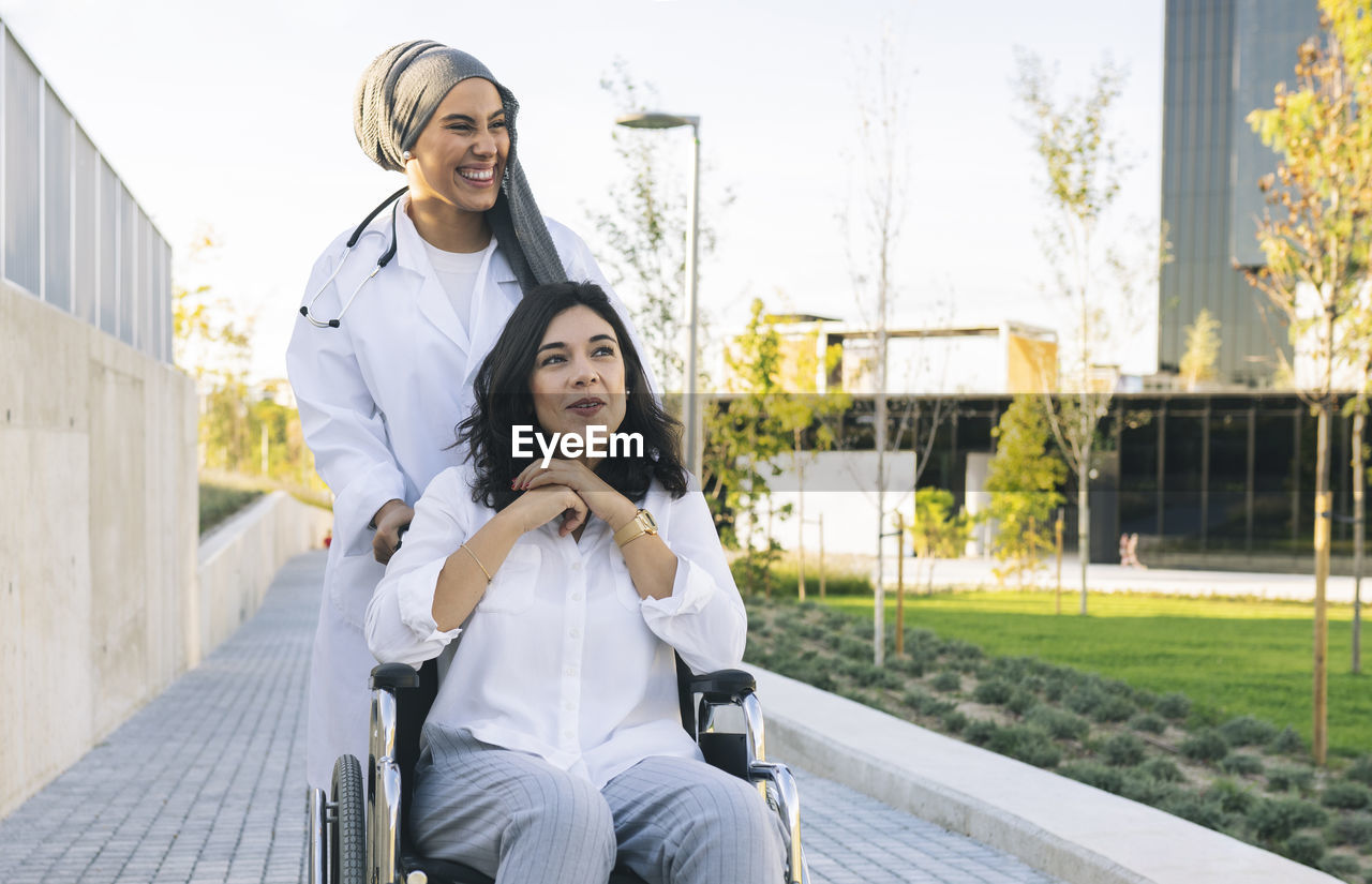 Cheerful female healthcare worker standing behind disabled woman sitting on wheelchair