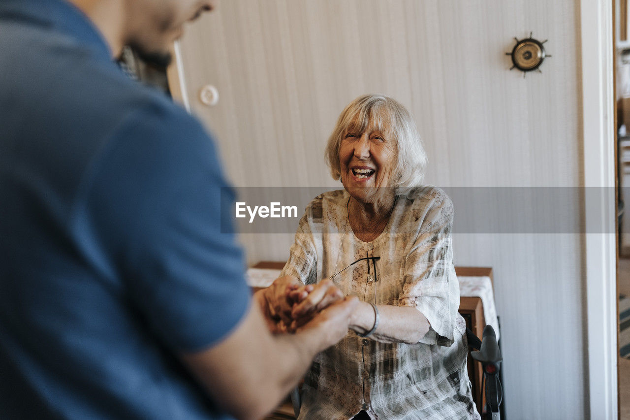 Happy senior woman holding hands of male care assistant at home