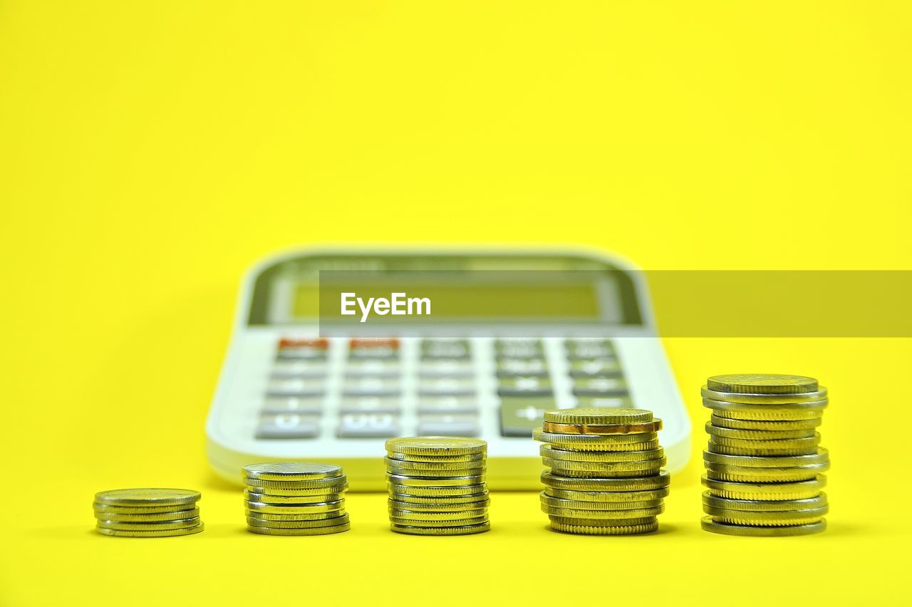 Close-up of coins with calculator on yellow background