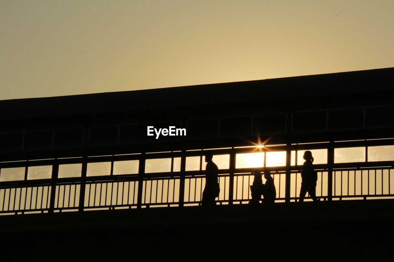 Low angle view of silhouette people on bridge against clear sky during sunset
