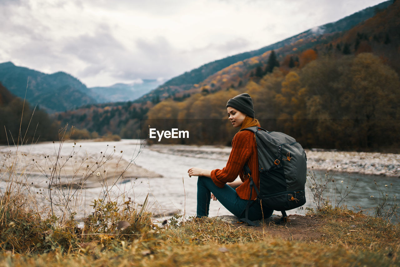 SIDE VIEW OF SENIOR MAN SITTING ON MOUNTAIN AGAINST SKY