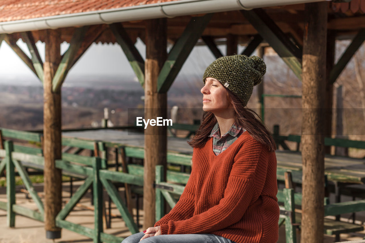 Woman with eyes closed sitting against empty table and chairs