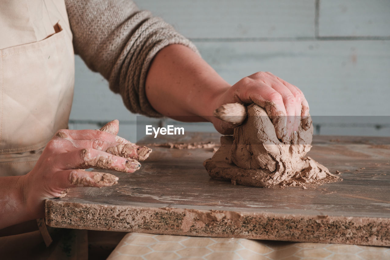 Midsection of person kneading clay on table